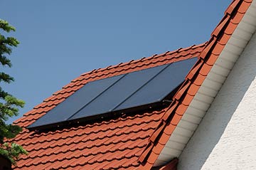 Solarpanele auf dem mit roten Pfannen eingedeckten Dach eines Wohnhauses.
